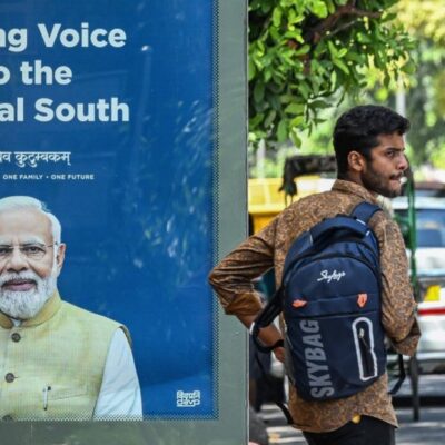 Pedestre aguarda em ponto de ônibus exibindo o retrato do primeiro-ministro da Índia, Narendra Modi, em Nova Délhi