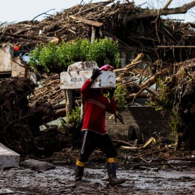 Um homem caminha com seus pertences por uma rua coberta de lama e detritos após um ciclone em Muçum, Rio Grande do Sul