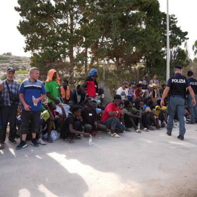 Policiais italianos diante de migrantes sentados no porto da ilha italiana de Lampedusa, em 16 de setembro de 2023