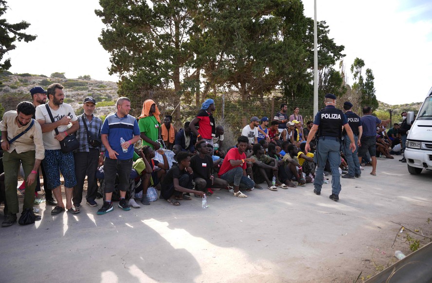 Policiais italianos diante de migrantes sentados no porto da ilha italiana de Lampedusa, em 16 de setembro de 2023