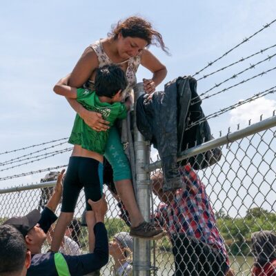 Uma mãe ajuda seu filho a pular a cerca de arame farpado em Eagle Pass, Texas, após cruzar para os EUA vindo do México em 25 de agosto de 2023