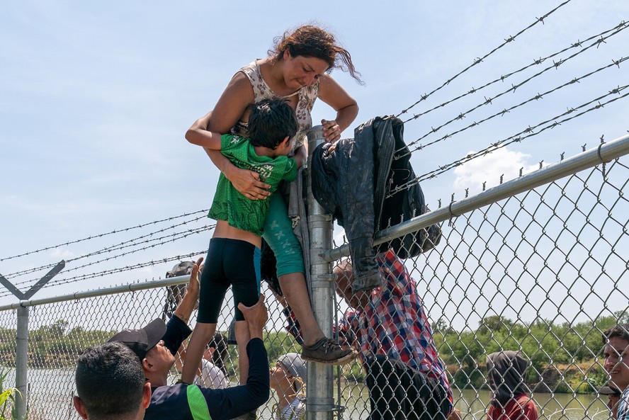 Uma mãe ajuda seu filho a pular a cerca de arame farpado em Eagle Pass, Texas, após cruzar para os EUA vindo do México em 25 de agosto de 2023
