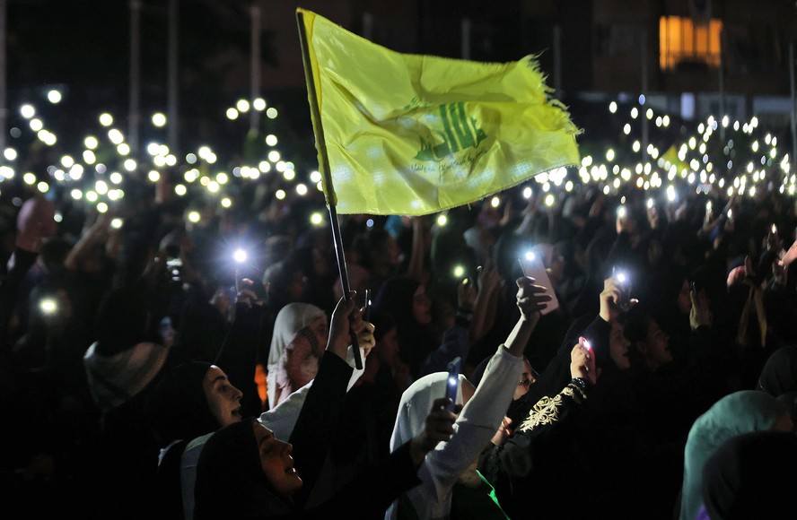 Apoiadores do Hezbollah seguram seus telefones e agitam a bandeira do partido durante uma celebração que marca o 40º aniversário da criação do movimento xiita no subúrbio sul de Beirute