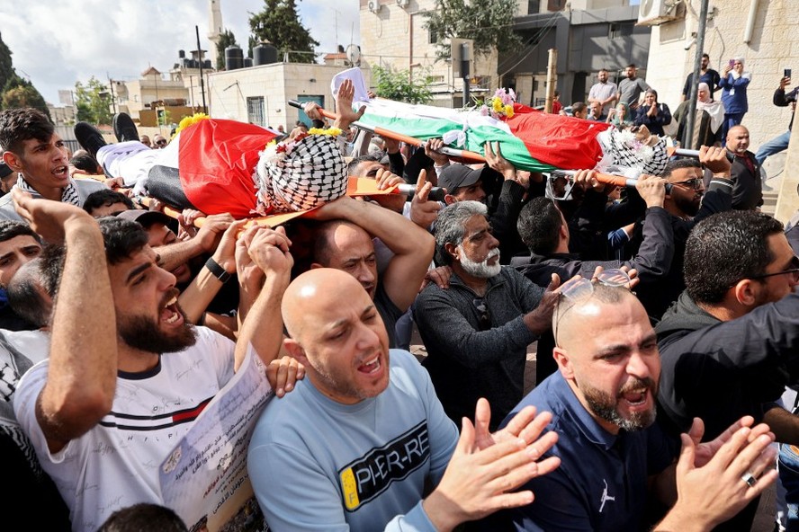 Homens carregam os corpos envoltos em bandeiras de dois jovens palestinos mortos em confrontos com colonos e forças israelenses na Cisjordânia