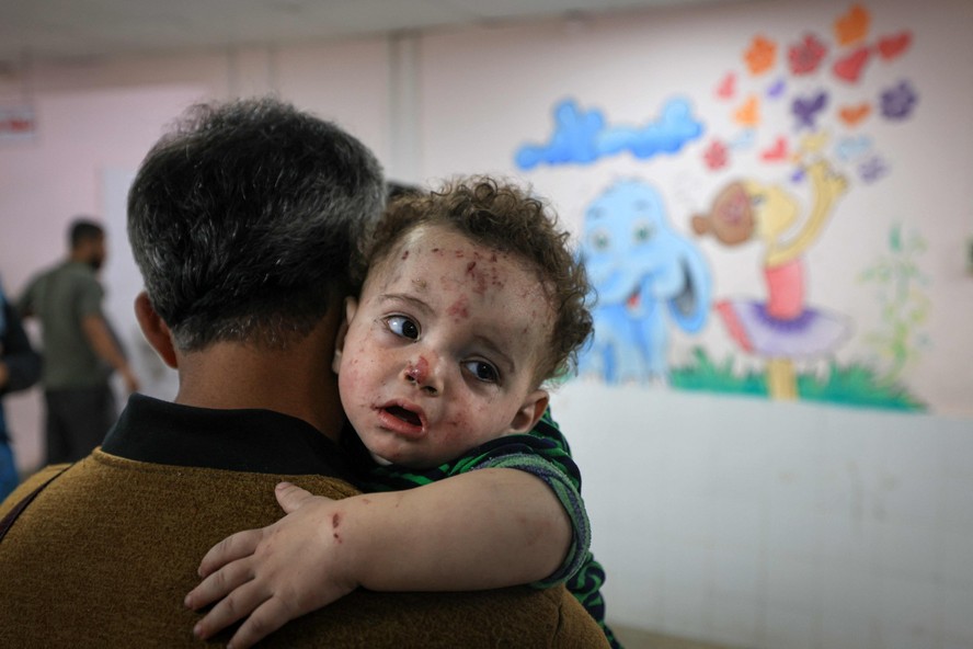 Homem segura criança ferida após bombardeio a campo de refugiado no hospital al-Quds, em Gaza