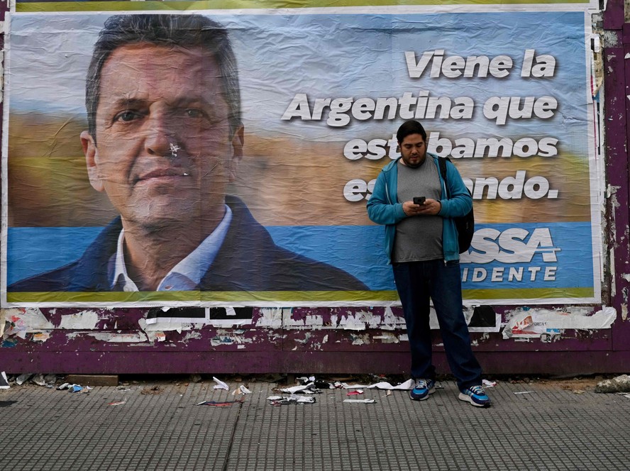 Homem olha telefone diante de cartaz do candidato à Presidência da Argentina Sergio Massa