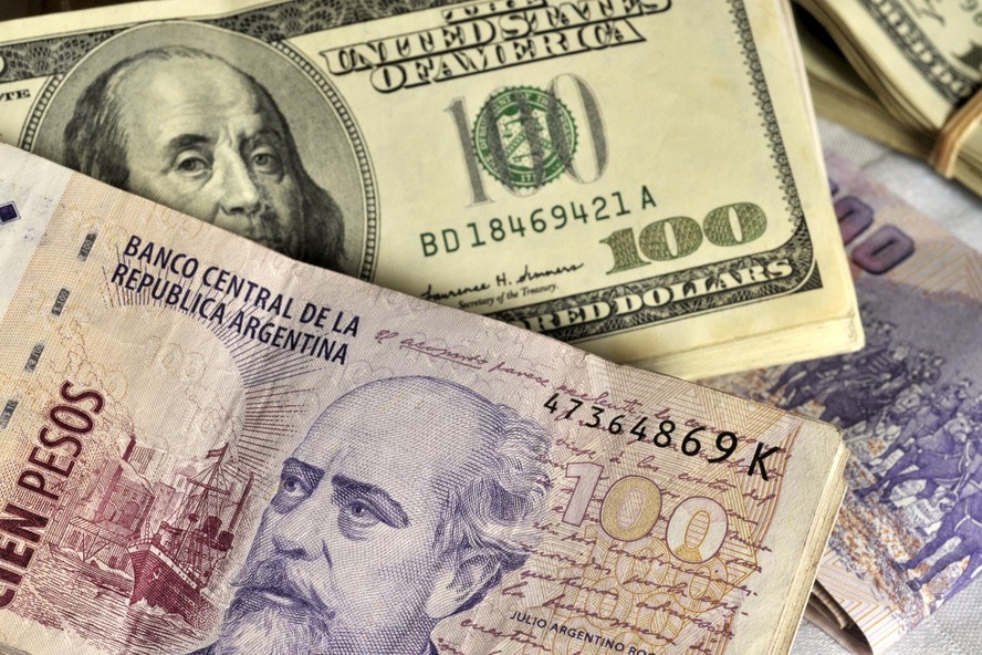 Pilhas de notas de 100 pesos argentinos e notas de 100 dólares americano: governo elevou cotação do dólar para exportadores