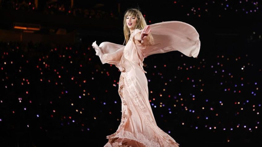 A cantora Taylor Swift vestida em um vestido cor-de-rosa claro, durante apresentação em palco