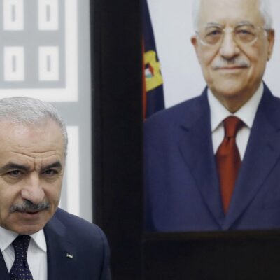 O primeiro-ministro palestino, Mohammad Shtayyeh, ao lado de um retrato do presidente da Autoridade Nacional Palestina, Mahmud Abbas