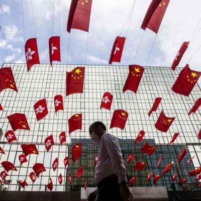 Homem caminha sob uma exibição das bandeiras de Hong Kong e da China no distrito de Tsim Sha Tsui, em Hong Kong