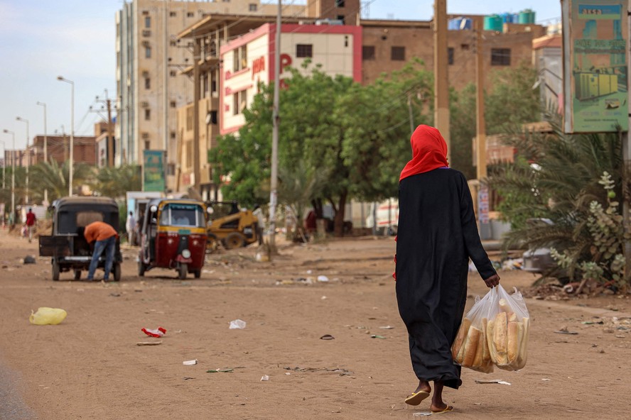 Mulher caminha com sacos de pão por uma rua em Cartum, capital do Sudão