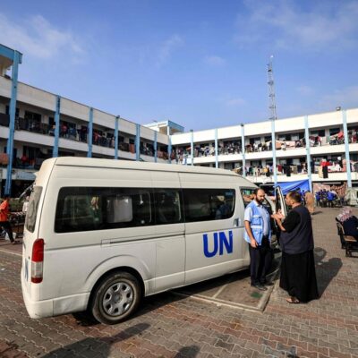 Um homem fala com um funcionário da Agência das Nações Unidas de Assistência e Obras para os Refugiados da Palestina (UNRWA) do lado de fora de um de seus veículos estacionados no playground de uma escola administrada pela UNRWA que foi convertida em um abrigo para palestinos deslocados em Khan Yunis, em no sul da Faixa de Gaza