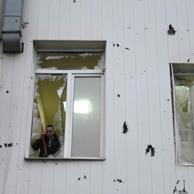 Mulher retira vidro quebrado de janela após bombardeio russo em Donetsk, no domingo