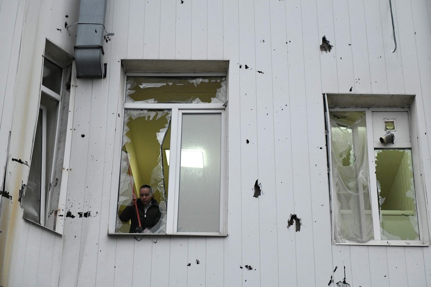 Mulher retira vidro quebrado de janela após bombardeio russo em Donetsk, no domingo