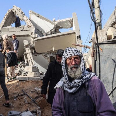 Idoso palestino observa enquanto homens vasculham escombros de casa destruída em ataque aéreo israelense durante a noite em Rafah, no sul da Faixa de Gaza
