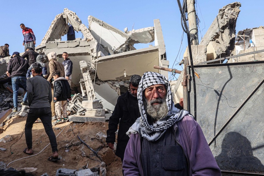Idoso palestino observa enquanto homens vasculham escombros de casa destruída em ataque aéreo israelense durante a noite em Rafah, no sul da Faixa de Gaza
