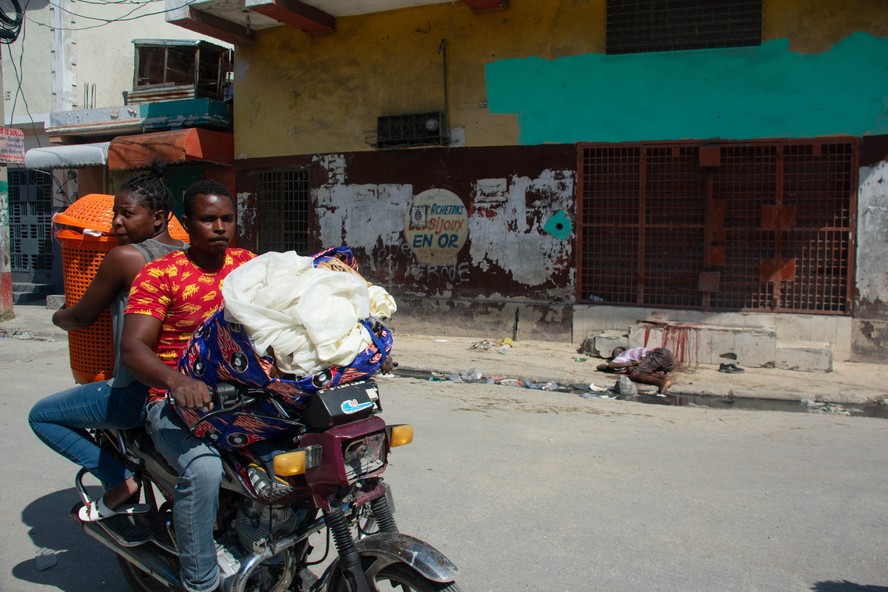 Moradores deixam suas casas enquanto a violência das gangues aumenta em Porto Príncipe, Haiti, e passam pelo corpo de uma vítima.