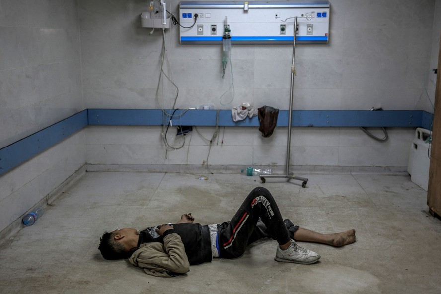 Jovem palestino ferido em bombardeio israelense deita-se no chão enquanto aguarda atendimento médico no hospital al-Shifa, na Cidade de Gaza