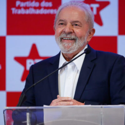 Lula sorri em frente a um painel vermelho e branco.