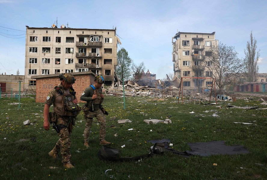 Oficiais de força policial especial caminham em frente a apartamentos destruídos por bombas aéreas durante a evacuação de moradores da vila de Ocheretine, não muito longe de Avdiivka, em Donetsk