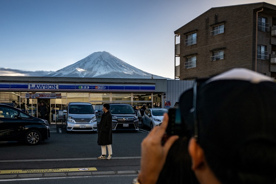 Turista posta em frente a uma loja de conveniência com o Monte Fuji ao fundo, na cidade de Fujikawaguchiko