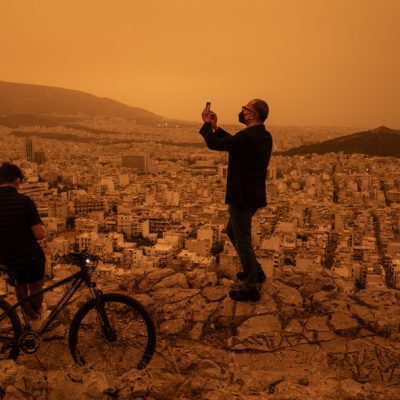 Um homem tira uma foto de Atenas a partir da colina Tourkovounia, após ventos do sul levarem ondas de poeira do Saara para a cidade