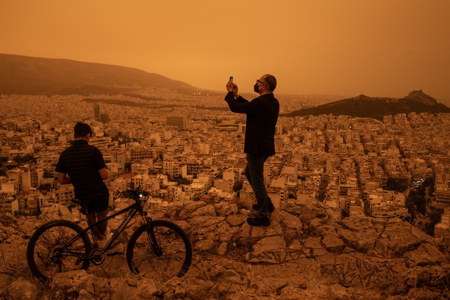 Um homem tira uma foto de Atenas a partir da colina Tourkovounia, após ventos do sul levarem ondas de poeira do Saara para a cidade