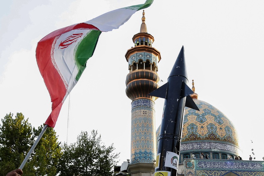 Iranianos levantam uma bandeira e a simulação de um míssil durante uma celebração após o ataque de mísseis e drones do Irã a Israel