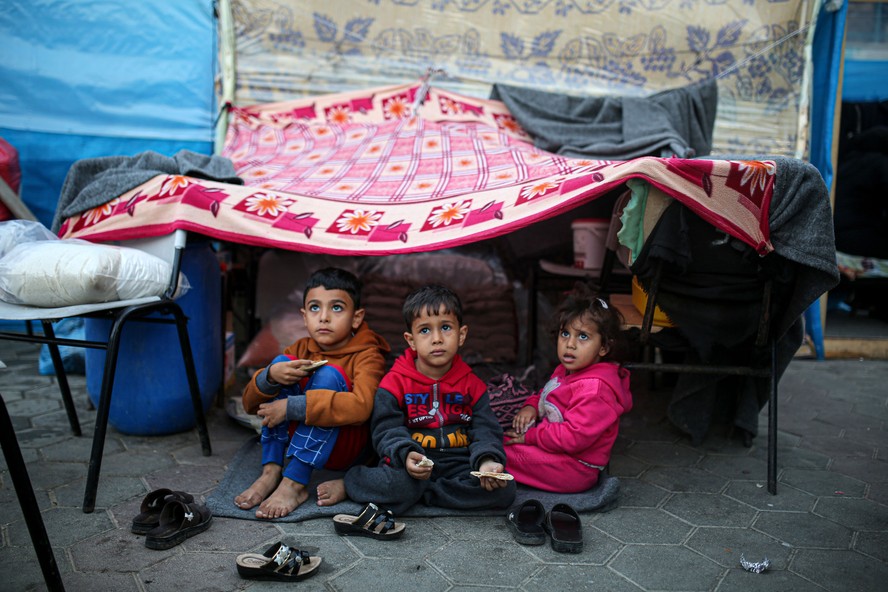 Crianças olham para o céu em um acampamento administrado pelas Nações Unidas para palestinos deslocados em Khan Younis, no sul da Faixa de Gaza