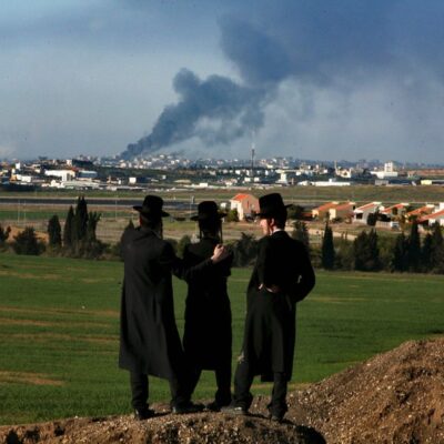 Três judeus ultraortodoxos contemplam coluna de fumaça que se aproxima de Gaza