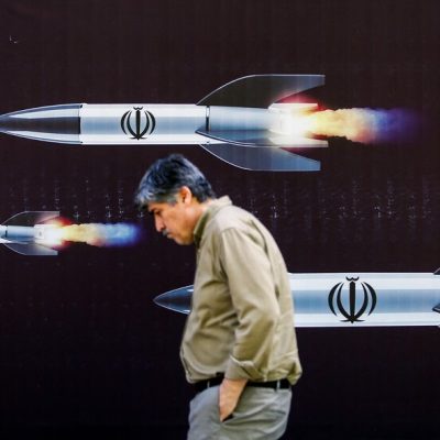 Homem passa por banner que retrata mísseis ao longo de uma rua em Teerã