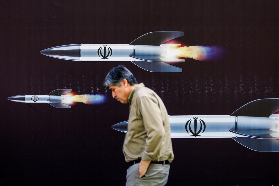 Homem passa por banner que retrata mísseis ao longo de uma rua em Teerã