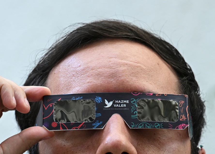 Homem testa os óculos de sol especiais para observar o próximo eclipse solar.