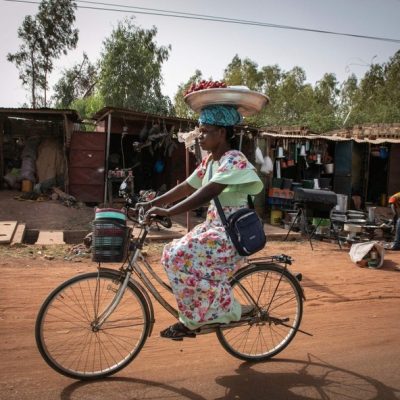Mulher equilibra prato de morangos na cabeça enquanto anda de bicicleta em Uagadugu, Burkina Faso