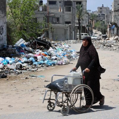 Mulher empurra cadeira de rodas na Cidade de Gaza