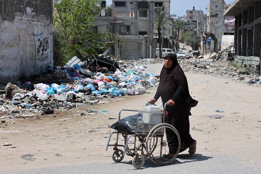 Mulher empurra cadeira de rodas na Cidade de Gaza