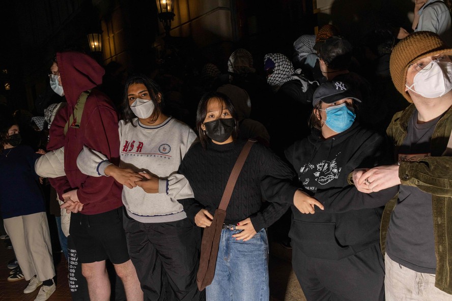 Estudantes/manifestantes cruzam os braços para proteger autoridades em potencial contra o alcance de colegas manifestantes que se barricaram dentro do Hamilton Hall,