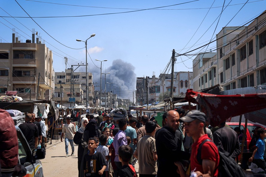Civis palestinos em rua de Rafah observam coluna de fumaça causada por bombardeio de Israel