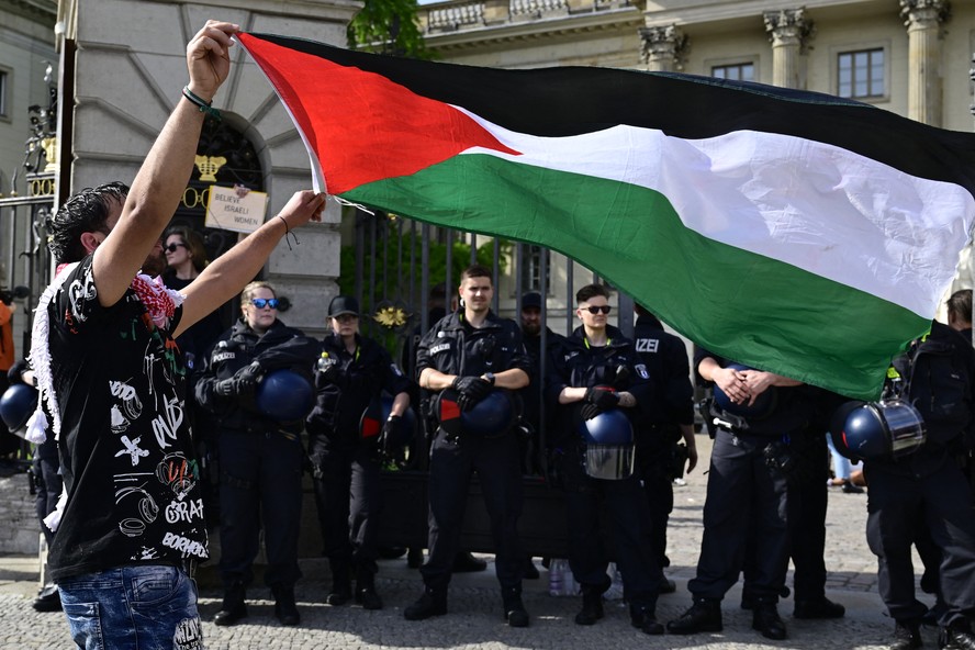 Manifestante exibe a bandeira da Palestina enquanto policiais bloqueiam a entrada a entrada da universidade após manifestação em solidariedade ao povo palestino em frente à Universidade Humboldt de Berlim.