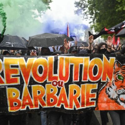 Os manifestantes seguram uma faixa com os dizeres 'Revolução ou barbárie' enquanto se manifestam contra o partido francês de extrema direita Rassemblement National (RN).