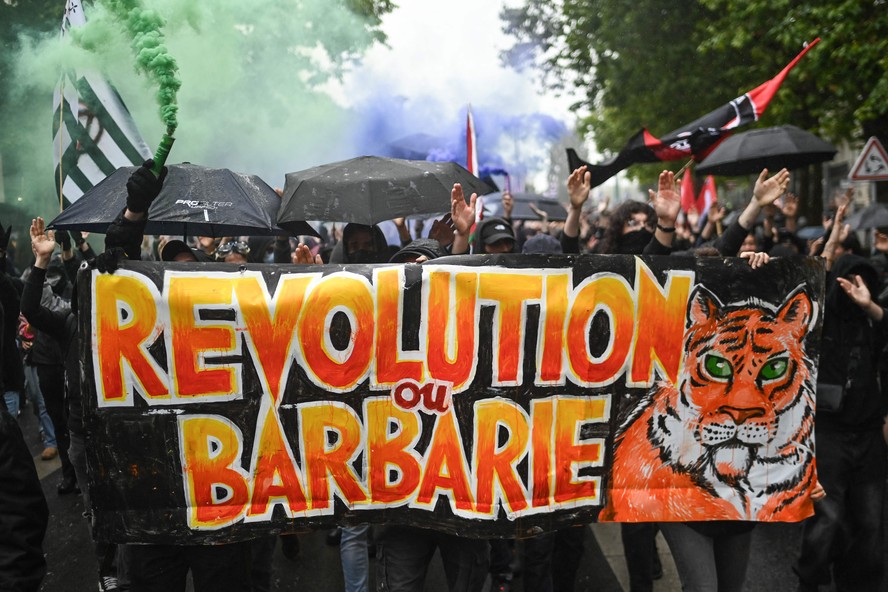 Os manifestantes seguram uma faixa com os dizeres 'Revolução ou barbárie' enquanto se manifestam contra o partido francês de extrema direita Rassemblement National (RN).