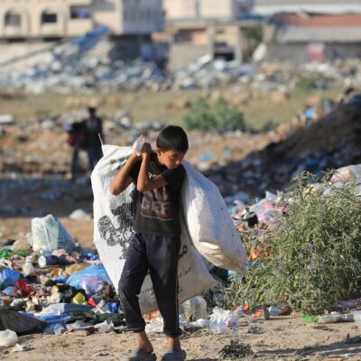 Jovem palestino carregando sacolas caminha perto de um depósito de lixo no campo de refugiados de al-Maghazi, no centro da Faixa de Gaza