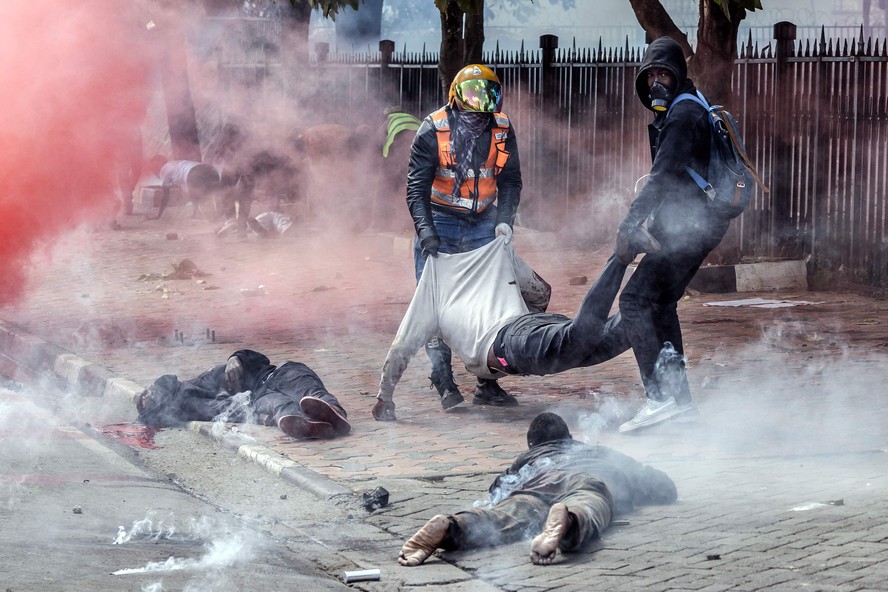 Manifestantes carregam um homem ferido enquanto outros estão caídos no chão em frente ao Parlamento do Quênia durante uma greve nacional para protestar contra o aumento de impostos e a Lei Financeira 2024 no centro de Nairóbi, em 25 de junho de 2024.