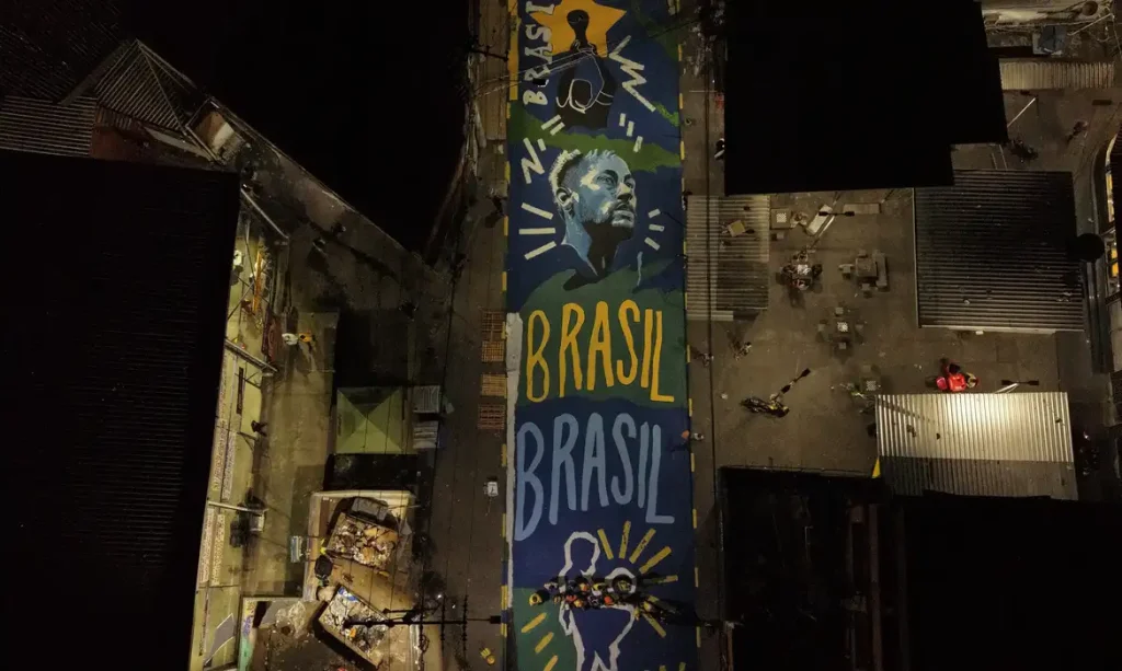 15/06/2026 - Rio de Janeiro - Pintura ressignifica rua marcada por operação letal no Rio de Janeiro. imagem aérea da rua pintada na penha com cores da seleção brasileira. Foto: Cadu Maia/Divulgação