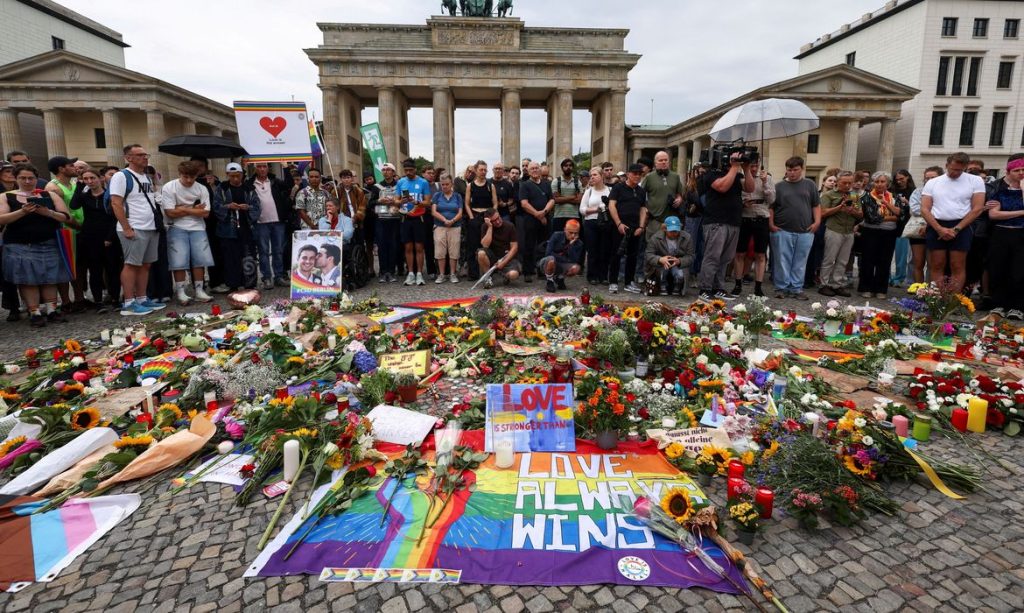 People gather around flowers, mementos and candles left by people at the Brandenburg Gate, after a deadly incident in which a vehicle crashed into a crowd near Berlin's annual Christopher Street Day Pride parade on Saturday evening, leaving multiple people injured and the parade called off, in Berlin, Germany, July 26, 2026. REUTERS/Christian Mang/Proibida Reprodução