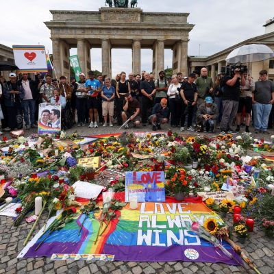 People gather around flowers, mementos and candles left by people at the Brandenburg Gate, after a deadly incident in which a vehicle crashed into a crowd near Berlin's annual Christopher Street Day Pride parade on Saturday evening, leaving multiple people injured and the parade called off, in Berlin, Germany, July 26, 2026. REUTERS/Christian Mang/Proibida Reprodução