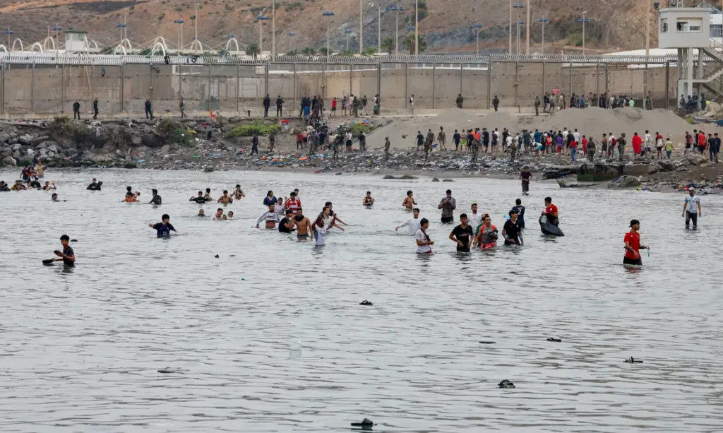 People waddle through water to enter Spain, and in the background people who just entered Spain return back to Morocco, amid mass crossings of migrants on foot and by sea from Morocco into Spanish territory, in Ceuta, Spain, July 31, 2026. REUTERS/Jon Nazca REFILE - CHANGES SLUG