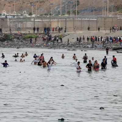 People waddle through water to enter Spain, and in the background people who just entered Spain return back to Morocco, amid mass crossings of migrants on foot and by sea from Morocco into Spanish territory, in Ceuta, Spain, July 31, 2026. REUTERS/Jon Nazca  REFILE - CHANGES SLUG