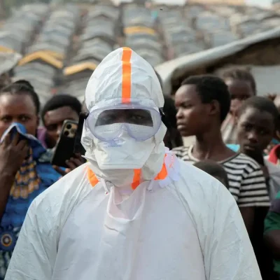 Profissional de saúde usando equipamento de proteção individual ao lado de pessoas deslocadas que aguardam enterro de vítimas com suspeita de Ebola no campo de deslocados de Kigonze, em Bunia, no leste da República Democrática do Congo
18 de junho de 2026 REUTERS/Gradel Muyisa Mumbere