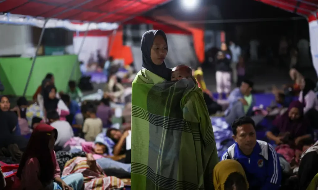 A woman holds a baby as people rest in a shelter at a makeshift evacuation center at a stadium in the aftermath of an earthquake, in Maumere, East Nusa Tenggara, Indonesia, August 16, 2026. REUTERS/Edgar Su/Proibido Reprodução